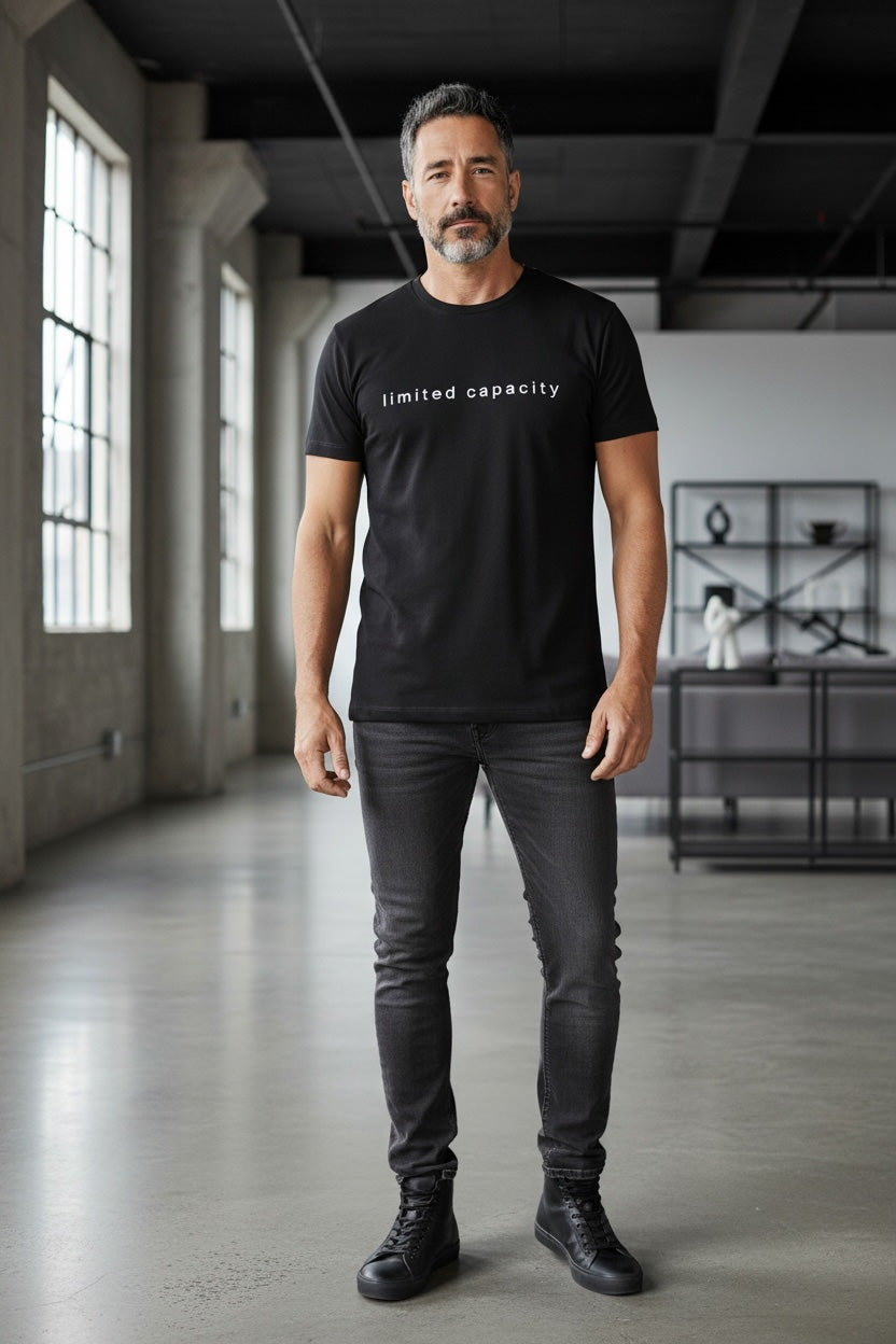 Man wearing a black t-shirt with 'limited capacity' text in a modern indoor setting.